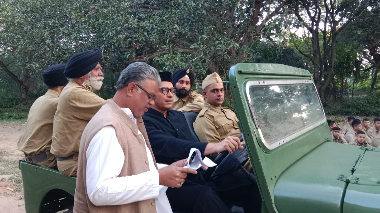 Director briefing an actor seated in a period jeep beside INA soldiers in uniform